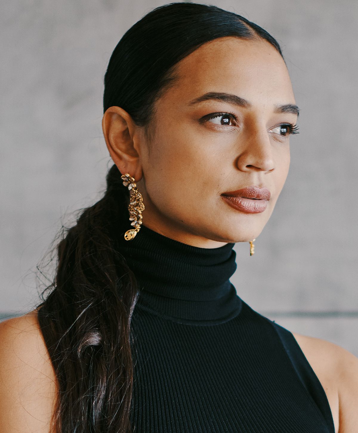 Woman in black turtleneck with statement earrings.