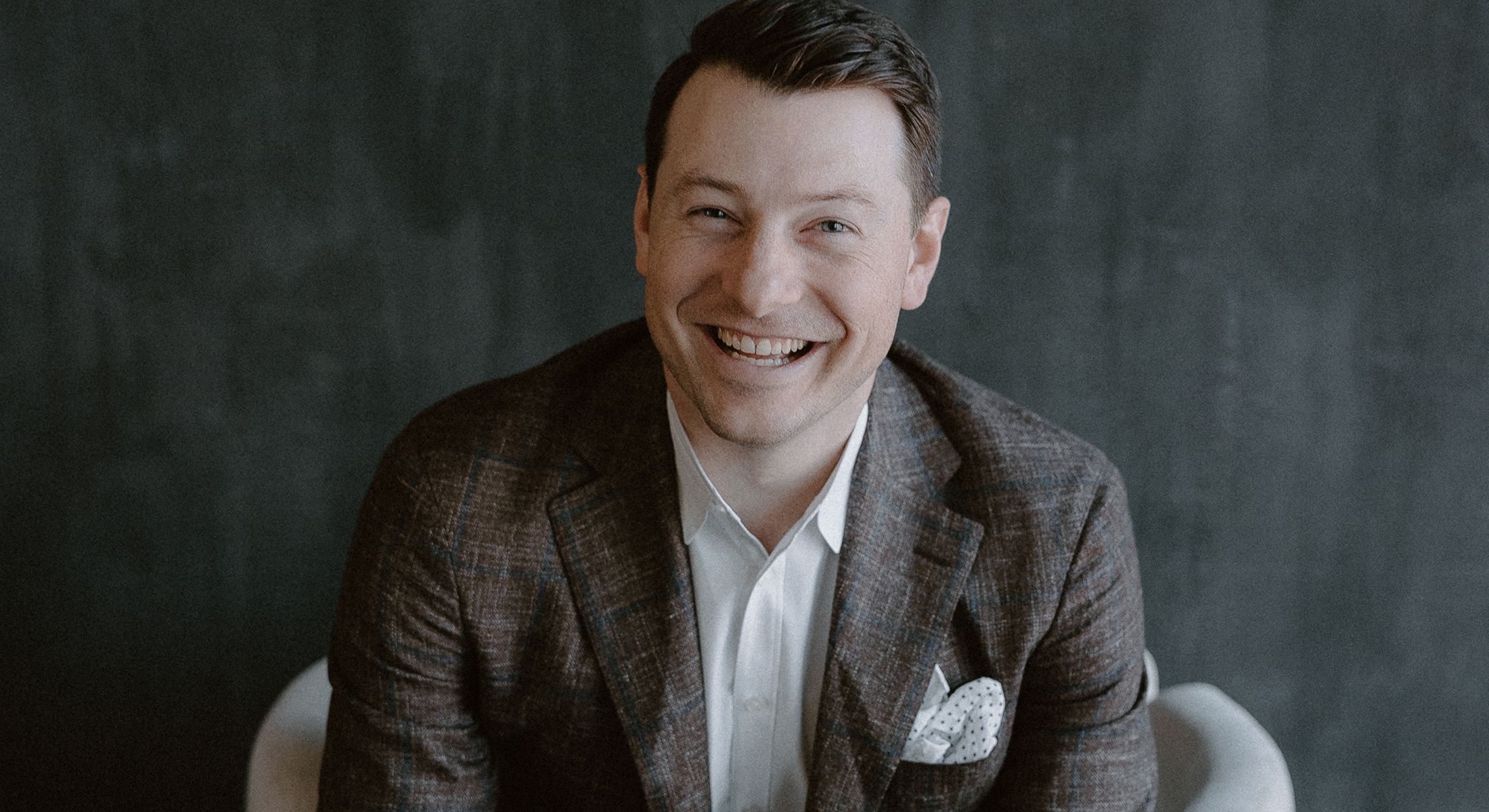 Smiling man in a brown plaid blazer.