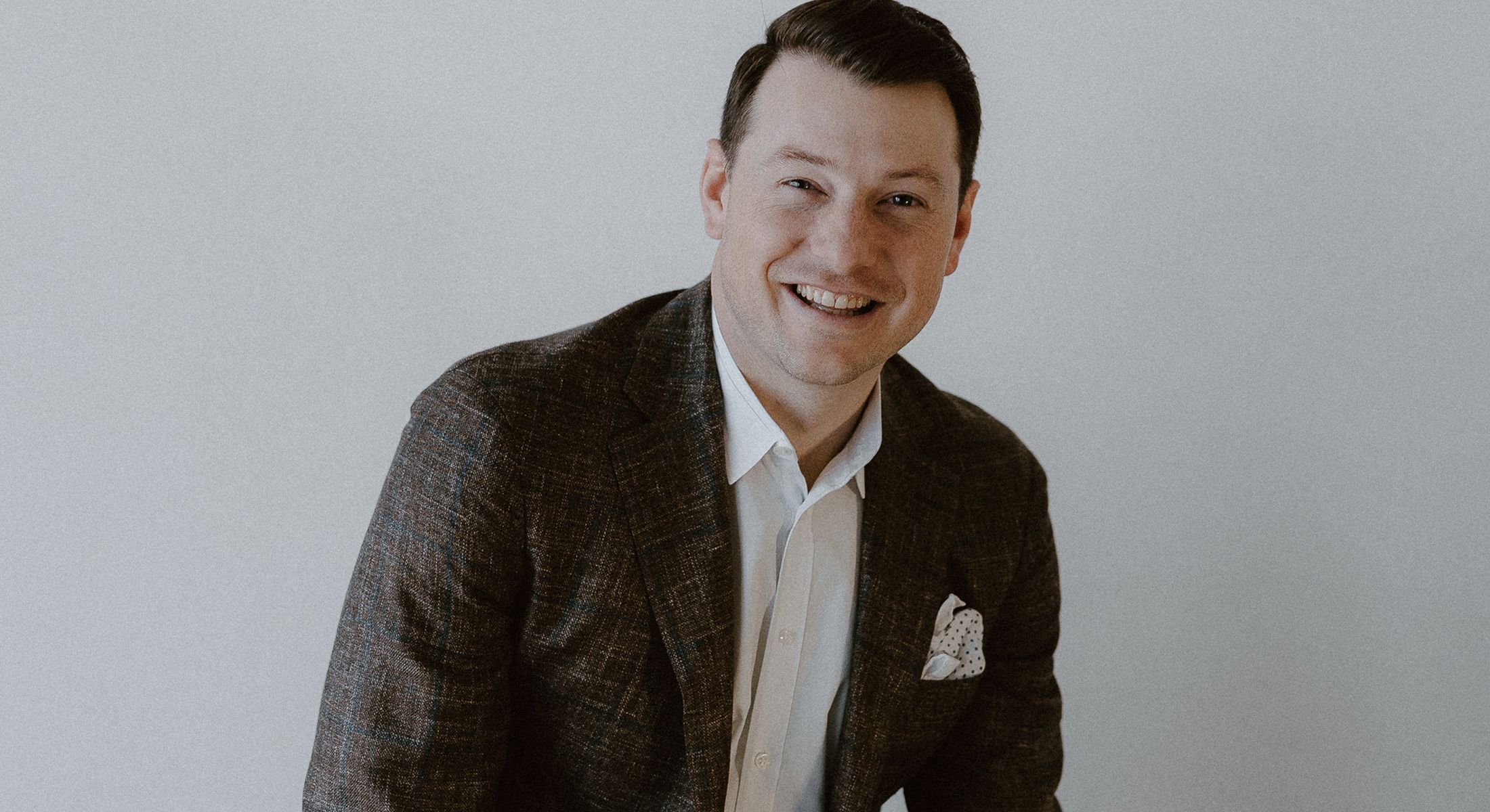Smiling man in formal attire against a neutral background.