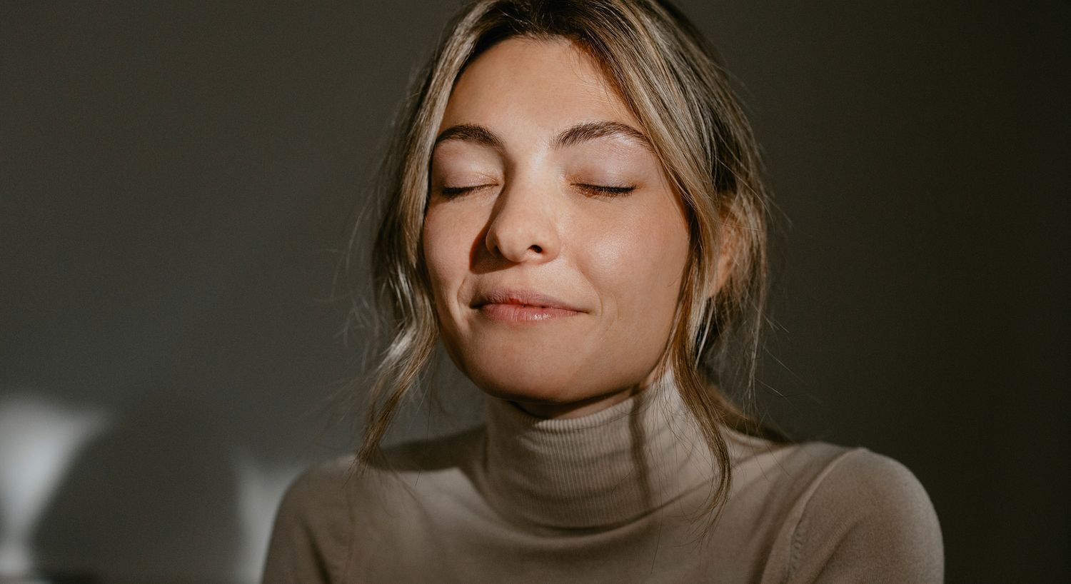 Woman with closed eyes, serene expression in light.